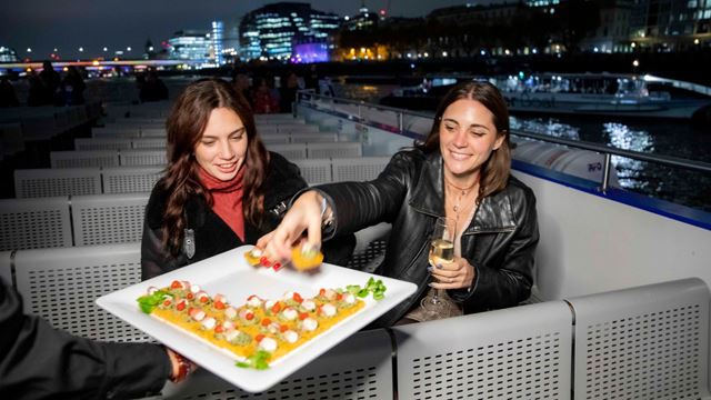 Two people sat on chairs outside on a river cruise taking canapes off a plate.
