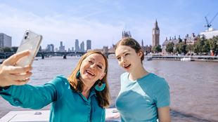 Two women are taking a selfie abord a City Cruises boat, with Big Ben on the background.