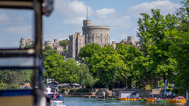 Machen Sie eine 40-minütige Bootstour an Bord des French Brothers Windsor Riverboat und bewundern Sie die fantastische Aussicht auf die königliche Stadt und Windsor Castle. © visitlondon.com/ Michael Barrow Aussicht vom Fluss auf Windsor Castle umgeben von grünen Blätterdach.