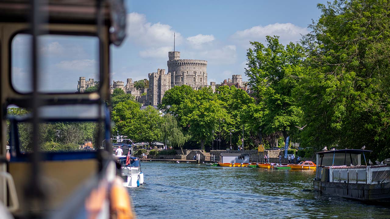 Blick vom Fluss auf Windsor Castle, umgeben von einem grünen Blätterdach.