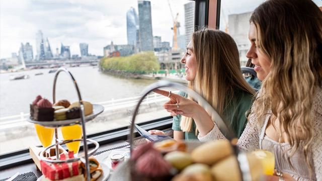 Two women eating afternoon tea on a bus with views of London