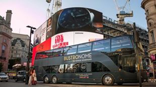 Un grand bus noir avec un plafond en verre est garé devant les écrans géants de Picadilly Circus à Londres.
