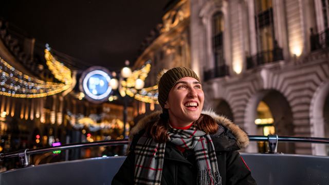 Une jeune femme se trouvant sur le pont supérieur du Christmas bus tour semble ravie par les décorations de Noël de Londres.