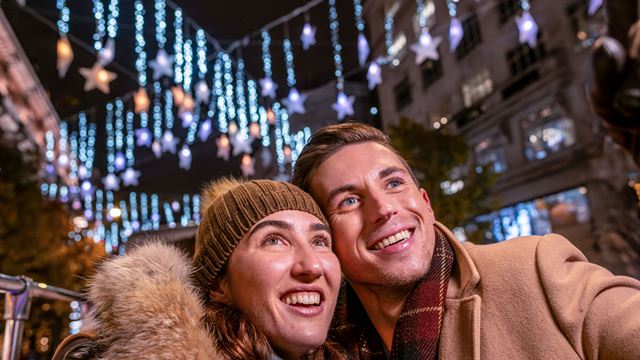 A man and a woman sit close together on the top deck of the Christmas Bus Tour, admiring the Christmas decorations.