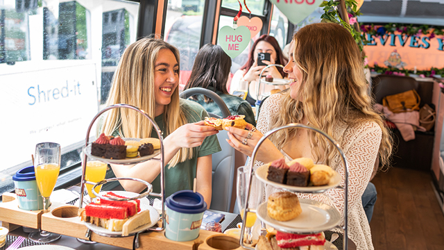 Deux femmes sont photographiées en train de prendre un afternoon tea à bord d'un bus panoramique de Londres et se délectent de scones tout en riant ensemble.