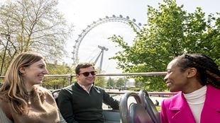 Un groupe de trois amis profitent d'une journée ensoleillée sur le pont supérieur du bus touristique Hop-On Hop-Off passant près du London Eye.