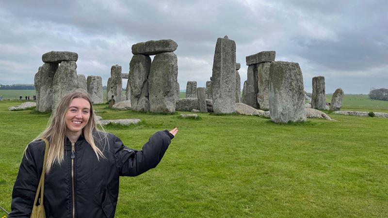 Person standing in front of Stonehenge pointing to rocks.