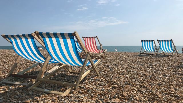 Blue and white striped deck chairs on pebbly Brighton beach on a sunny day.