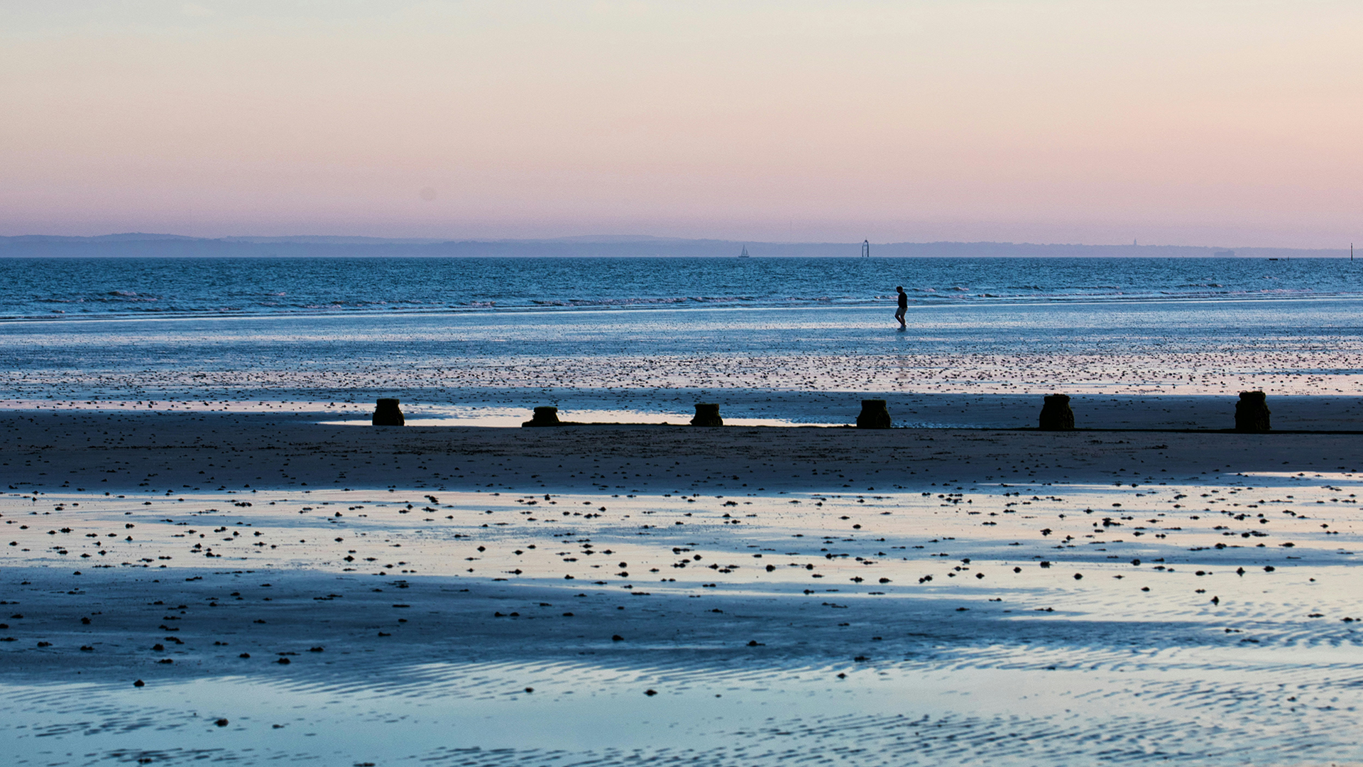 West Wittering beach in Chichester at sundown with a man walking in the distance.