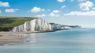 Photo of the White Cliffs at Seven Sisters National Park against the sea, with blue sky on the horizon.