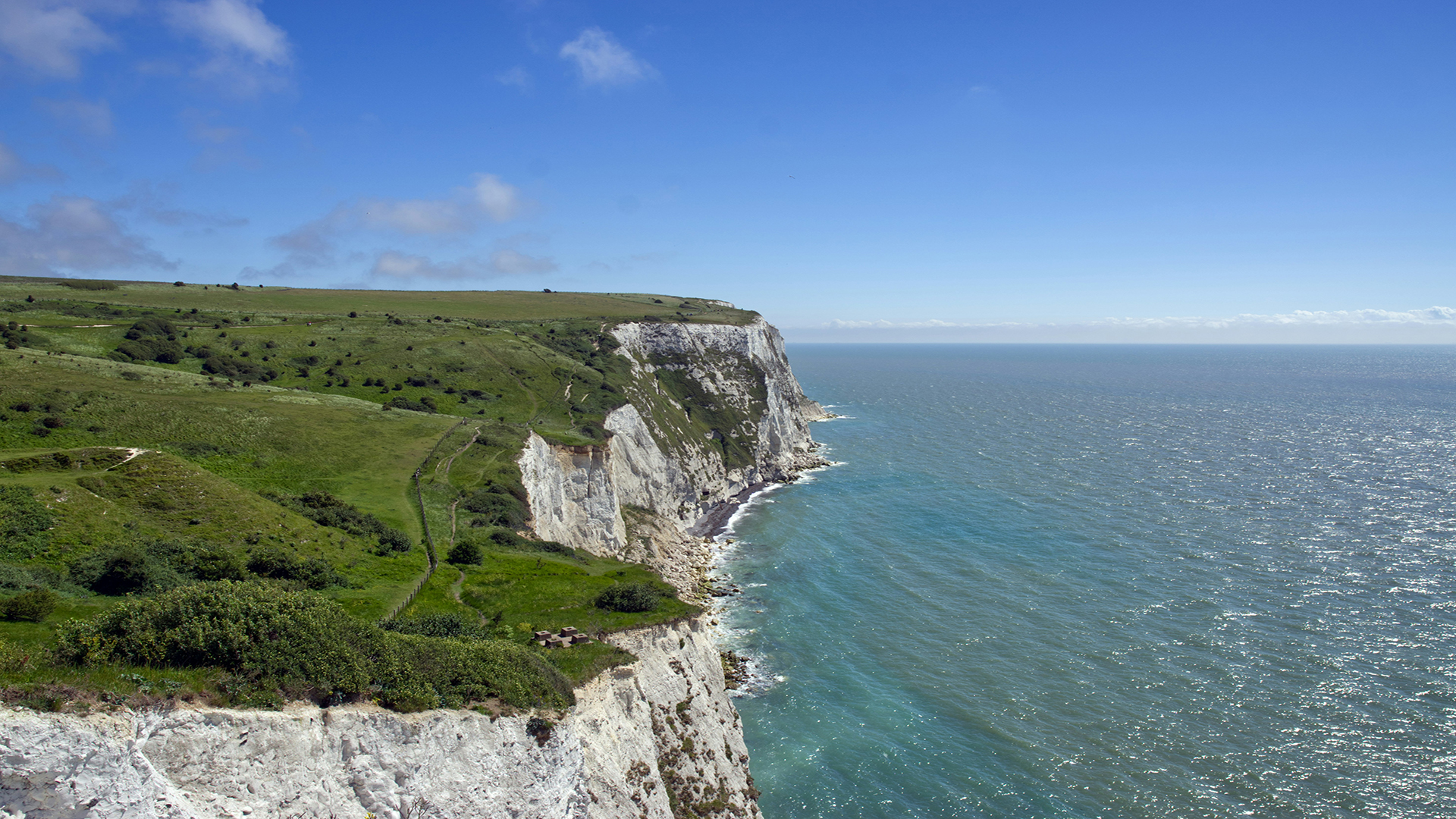 Visit the White Cliffs of Dover. Image courtesy of Unsplash, image credit: Darko M An areal image of the White Cliffs of Dover with the sea on a bright day.