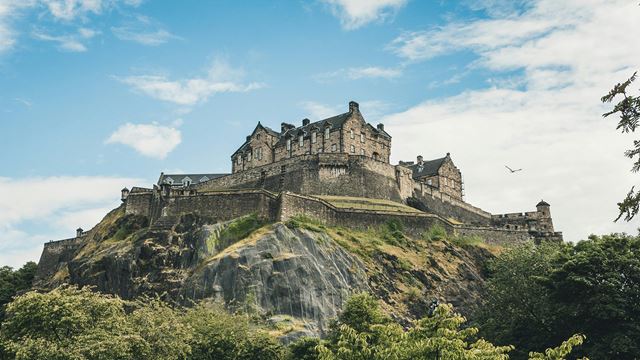 A view of Edinburgh castle with trees and bushes on a bright day. 