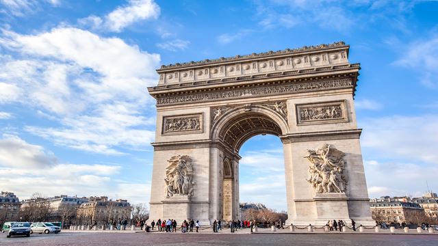  The Arc de Triomphe from afar with people walking around it on a bright day.