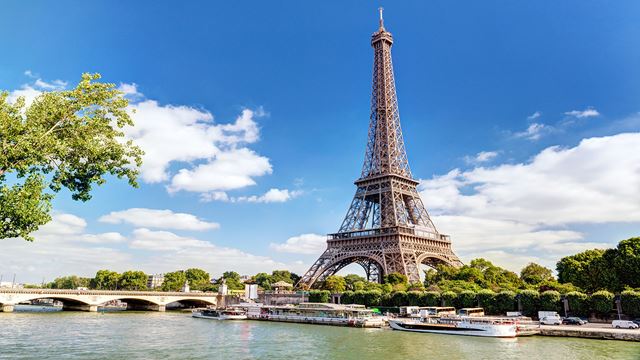 The river Seine with boats on it and the Eiffel Tower in the background on a sunny day.