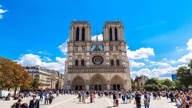 The facade of Notre Dame cathedral in Paris, with groups of people in the square in front.