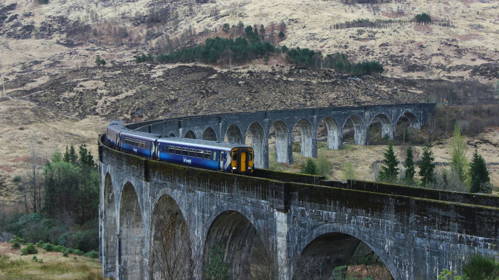Aerial view of a train travelling across a Scottish viaduct with hills in the background