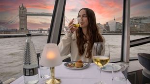 Person sitting at a table on a river cruise drinking a glass of wine.