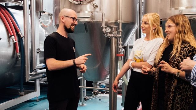 A group of people stand next to the machines of a brewhouse at Camden Town Brewery in London.