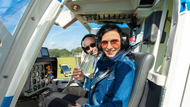 Un vol en hélicoptère au champagne © Adventure 001. Image reproduite avec l'aimable autorisation d'Adventure 001. Une femme est assise sur le siège du copilote, à côté du pilote, avec une coupe de champagne.