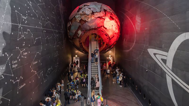 Uncover geological wonders at the Natural History Museum. Image credit: London & Partners/ Michael Barrow. Escalator at The Natural History Museum leading into a meteor sculpture to the Geological Museum.