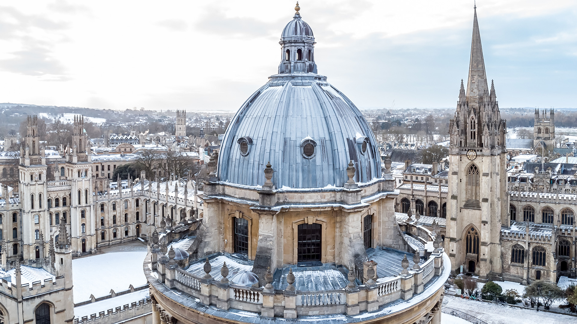 Visit Oxford on a day trip from London. Image courtesy of Golden Tours/Shutterstock. The Radcliffe Camera at Bodleian Library in the forefront and one of the colleges of the University of Oxford in the background all covered in a little snow.