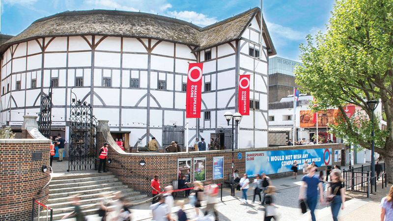 This outdoor view of the Shakespeare Globe Theatre shows passers-by walking along the street bordering the thatched-roofed venue. Head to the Globe to experience outdoor theatre as it was in Elizabethan times. Image courtesy of The Shakespeare Globe.