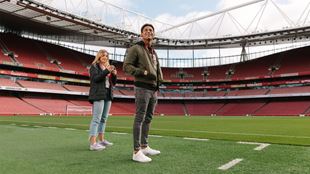 Two people standing on the pitch at Arsenal Stadium.