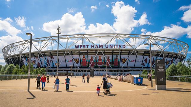 An exterior view of London Stadium on a bright day, showing the stadium bowl and the wording West Ham United on the side.