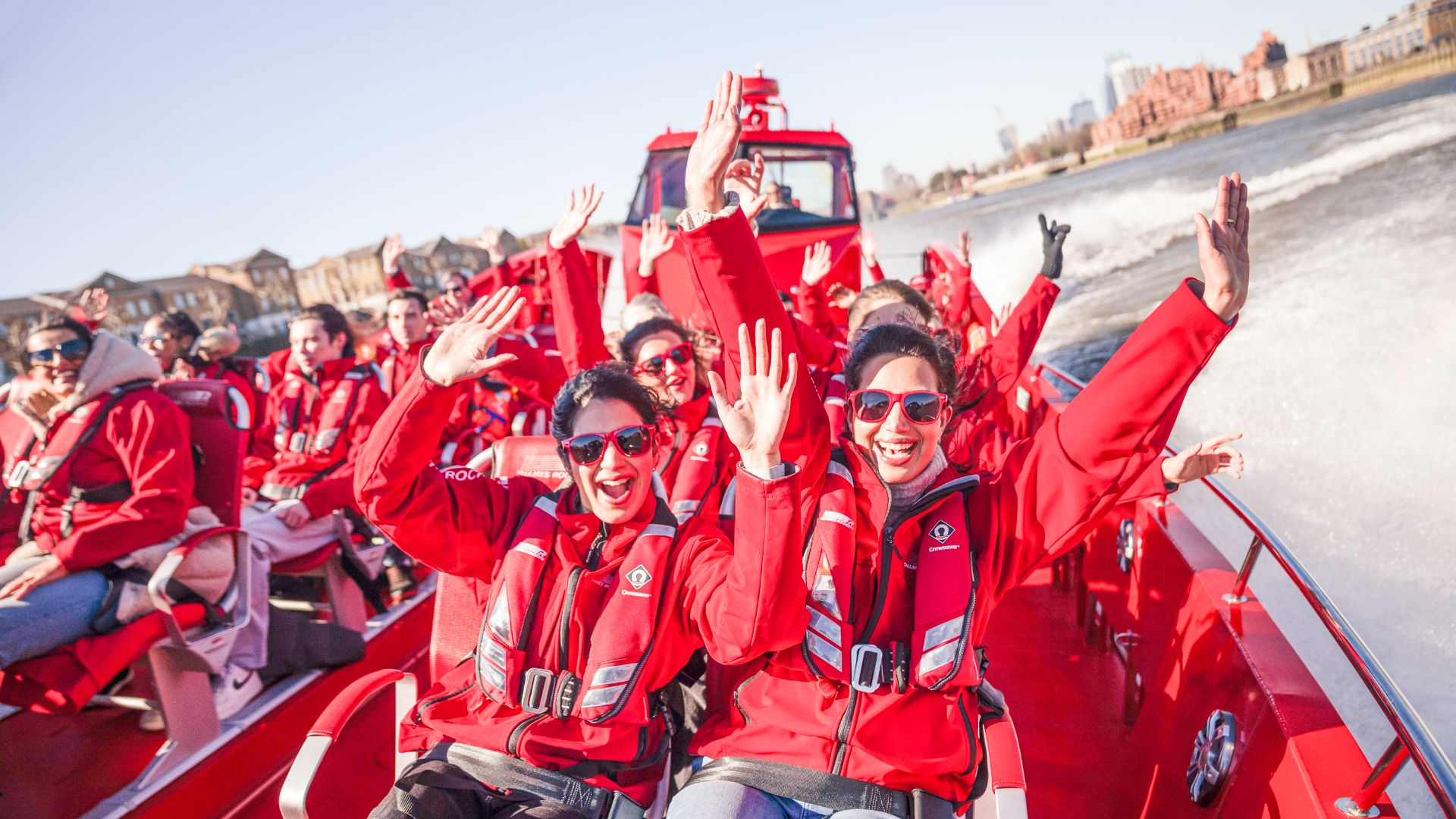 Hold on tight and race along the Thames with front-row views of London. Image courtesy of Thames Rockets. Group wearing red jackets on a high-speed boat ride along the River Thames, smiling and raising their hands.