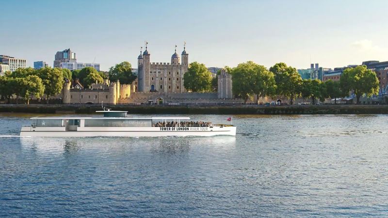 Discover London's rich history on a Tower of London River Cruise. Credit: Golden Tours. Image courtesy of Golden Tours. Tower of London River Cruise with white exterior and wide glass windows with the Tower of London in the background.