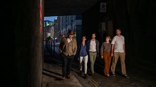 A group is led by a tour guide on a Jack The Ripper guided walk through a dark alleyway in East London.
