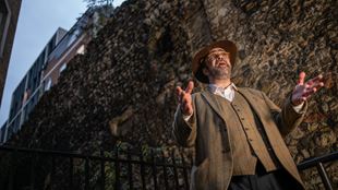 A man dressed of a tweed suit and wearing a brown hat is leading a Jack The Ripper tour in London.