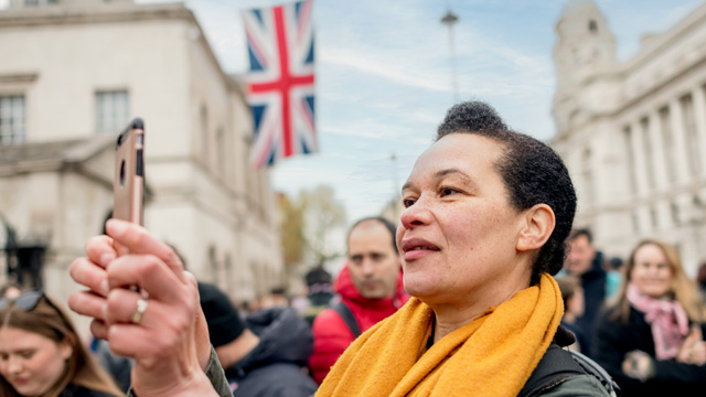 Nimm an der Royal Walking Tour of London teil und entdecke königliche Paläste udn andere Residenzen der Königsfamilie. Bild © visitlondon.com. Nahaufnahme einer Frau die einen gelben Schal trägt und ein Bild mit Ihrem Handy während einer geführten Tour macht.