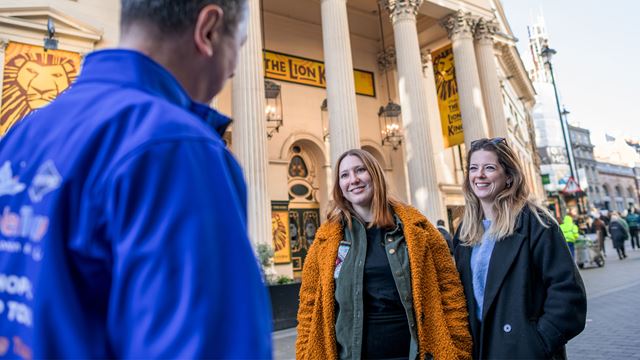 Tour guide speaking to two people with Lion King playing at Lyceum Theatre in the background.