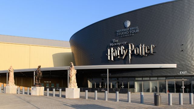 Das große schwarze Gebäude der Harry Potter Studios mit großen Statuen davor und strahlend blauem Himmel.