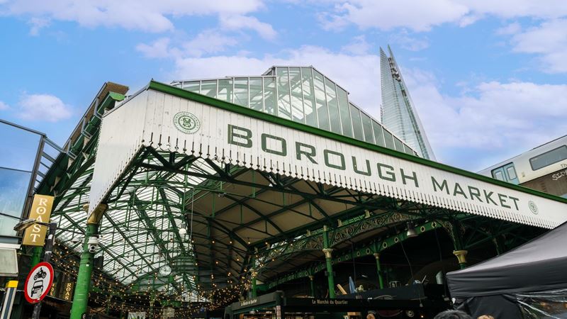Explore Borough Market, a historical market in Southwark. Image credit: London & Partners/Michael Barrow. Image courtesy of London & Partners/Michael Barrow. low angle photo taken of the Borough Market sign, with the tip of the Shard in the background