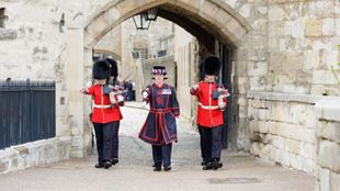 Warders dressed in black and red march through the tower of london.