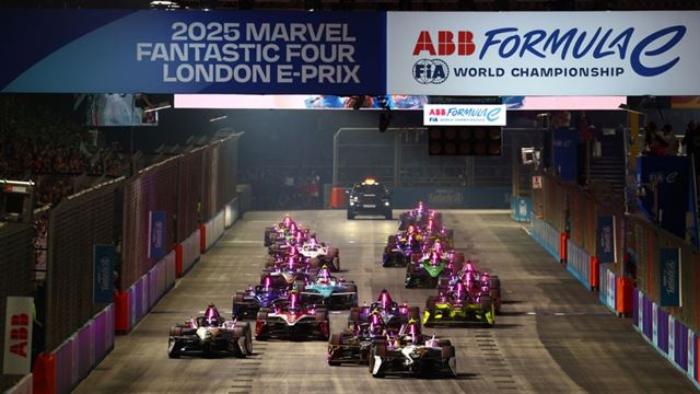 Formula E race cars line up on the starting grid during the London E-Prix at ExCeL London, racing on the championship's unique indoor-outdoor circuit beneath the event gantry.
