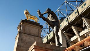 A statue of a rugby player after kicking a ball, and a gold lion statue.