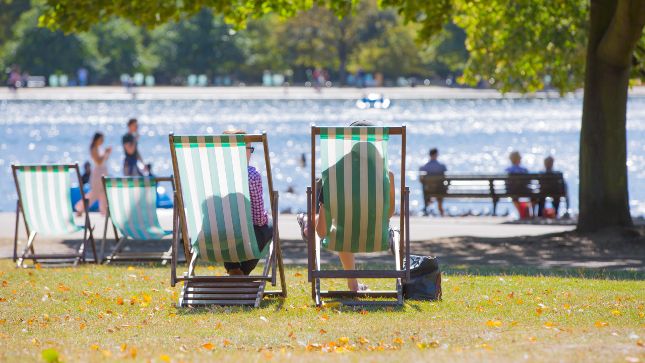 Two people sat on striped deck chairs in front of the lake at Hyde Park