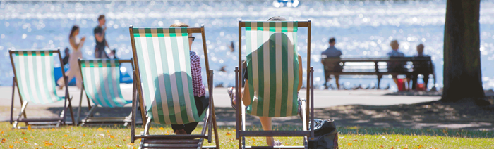 Two people sat on striped deck chairs in front of the lake at Hyde Park