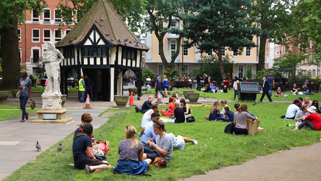 Groups of people sat on the grass in Soho Square socialising and eating picnics