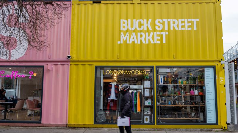 Stop off at Buck Street Market during your visit to Camden where you'll find independent fashion and food retailers. Credit: Shutterstock. Image courtesy of Shutterstock. Man walking past a bright pink and yellow shipping container with shops inside which has been converted into Buck Street Market