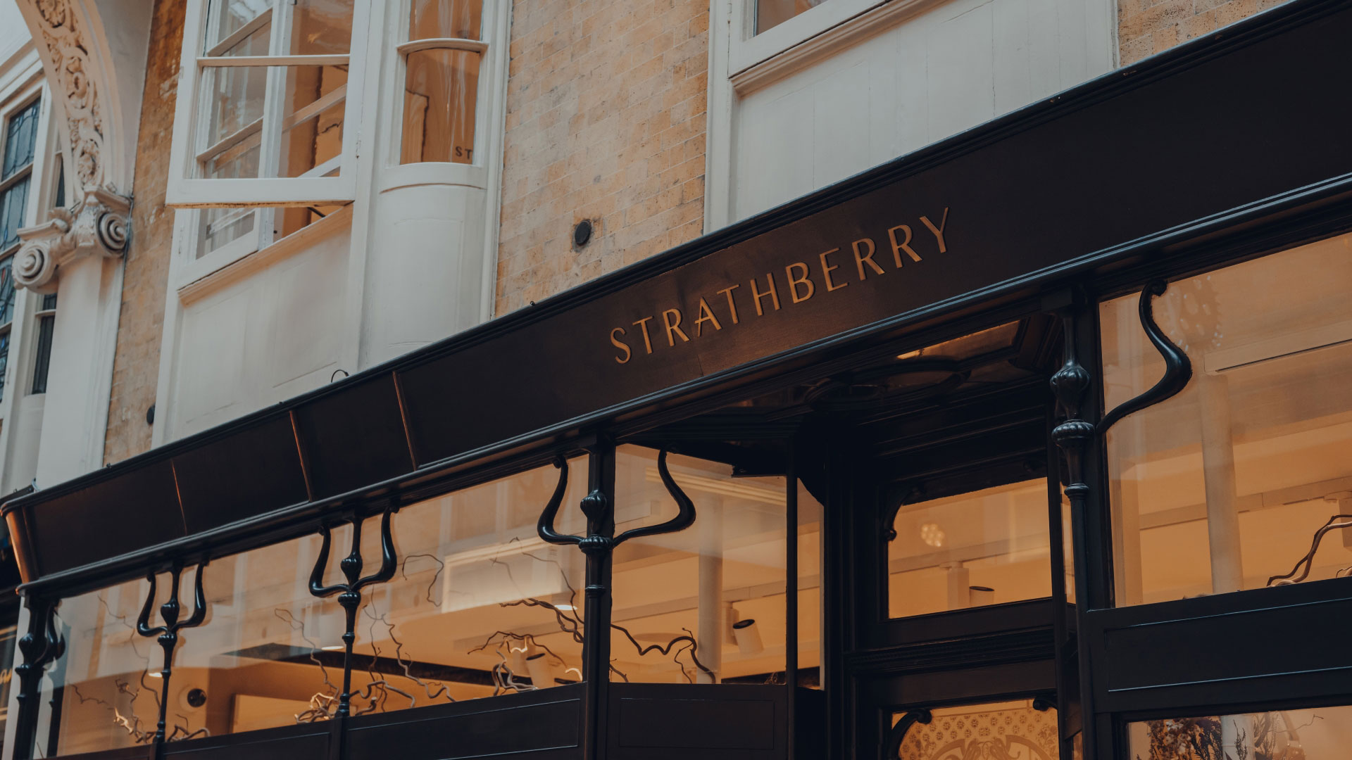 A black storefront lit up from inside with logo on the front spelling out Strathberry