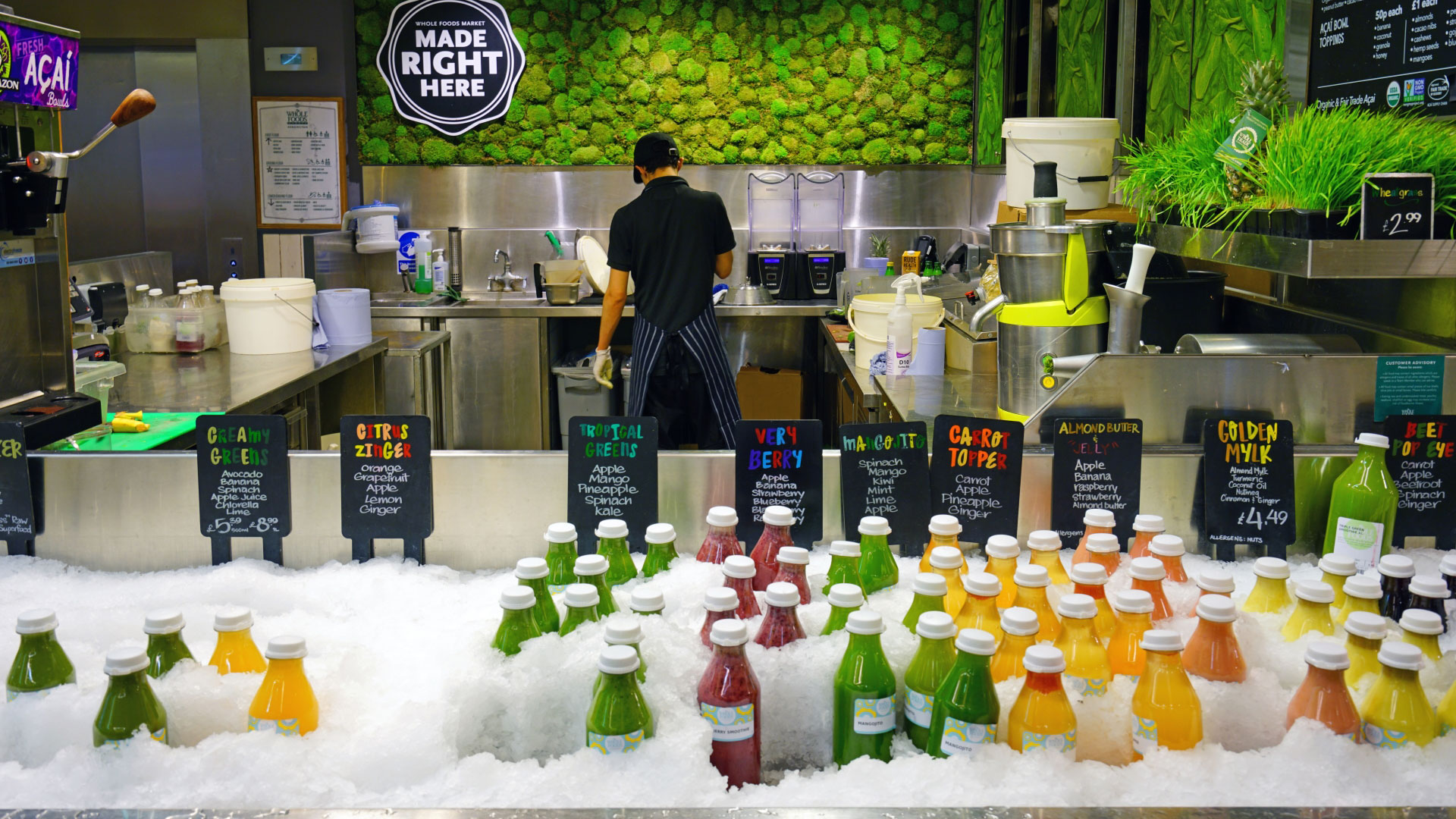 A juice station at Whole Foods Market with a person making fresh juice and a freezer with colourful juices ready to pick up in the foreground