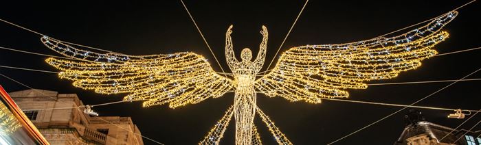high angle photo looking up at Christmas lights in the shape of an angel, with the night sky behind