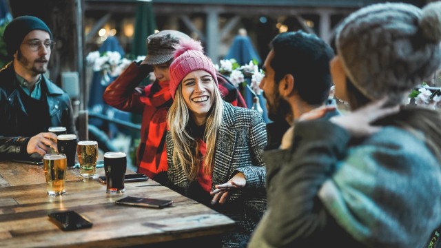 Freunde trinken am Abaend in einer Bar. Bild mit Genehmigung von © Shutterstock Freunde sitzen in Winterkleidung um einen Tisch mit Bier auf dem Tisch und lachen.