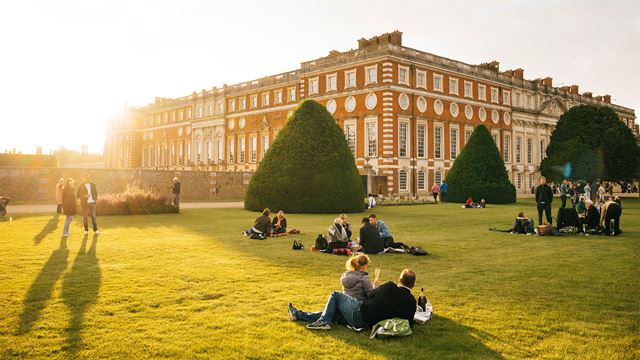 Crowds picnic in the grounds of Hampton Court Palace at sunset