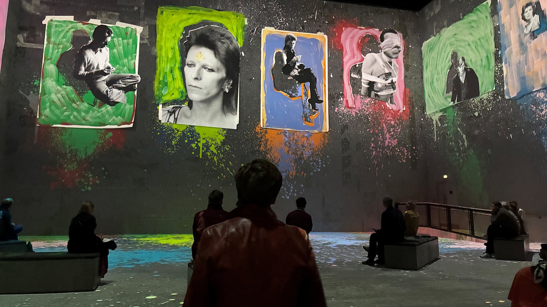 Six images of David Bowie surrounded by various colours on the screens at Lightroom, with audience members sitting in front of the screens.