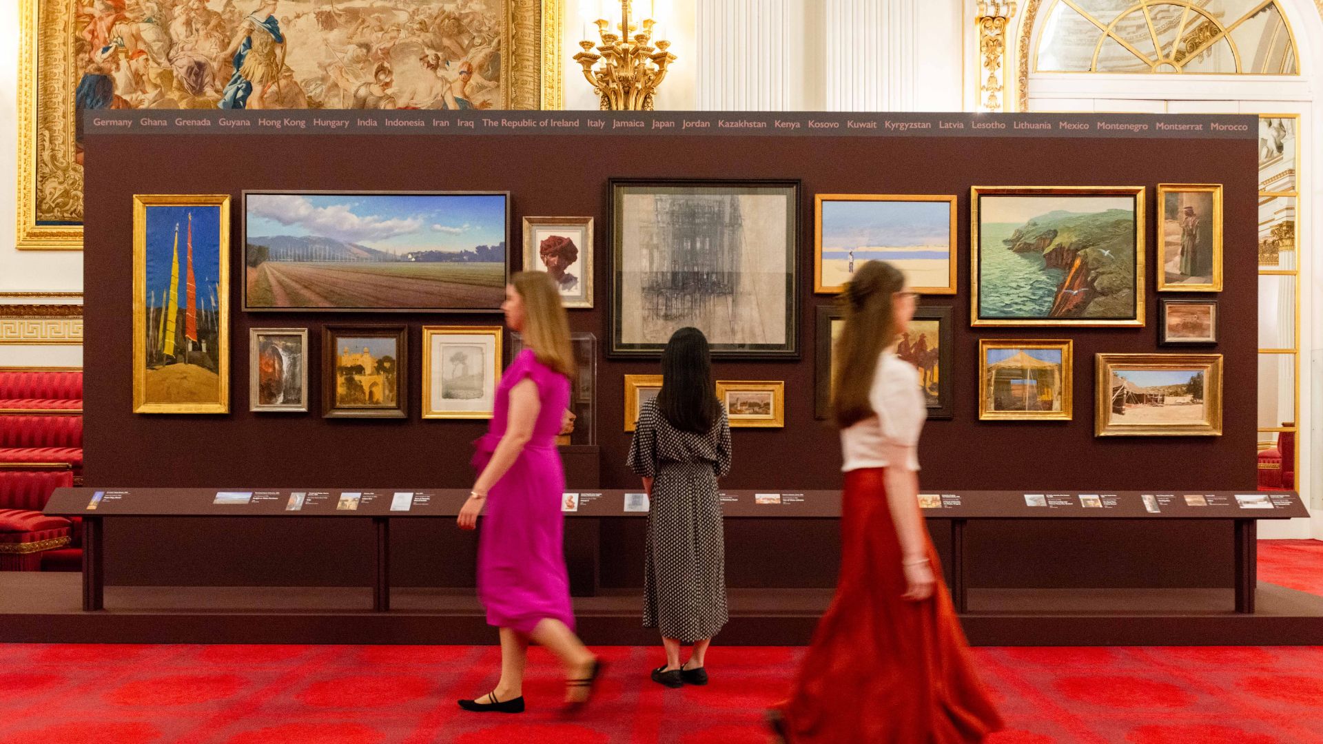 Explore more than 70 works of art from His Majesty The King’s private collection at The King’s Tour Artists. © Royal Collection Trust An exhibition wall at buckingham palace with people walking past the paintings.